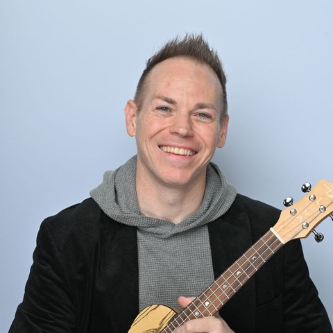 Ryan Today, smiling, holding a ukulele